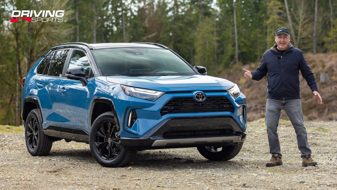 Un Toyota RAV4 Hybride blanc roulant sur une autoroute moderne avec des bâtiments en arrière-plan.