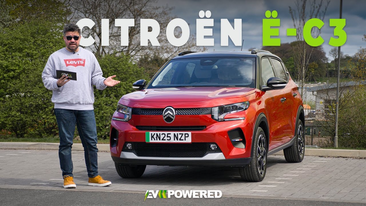 Une Citroën ë-C3 blanche roule sur une route sinueuse à travers des collines verdoyantes et des vignobles en France.