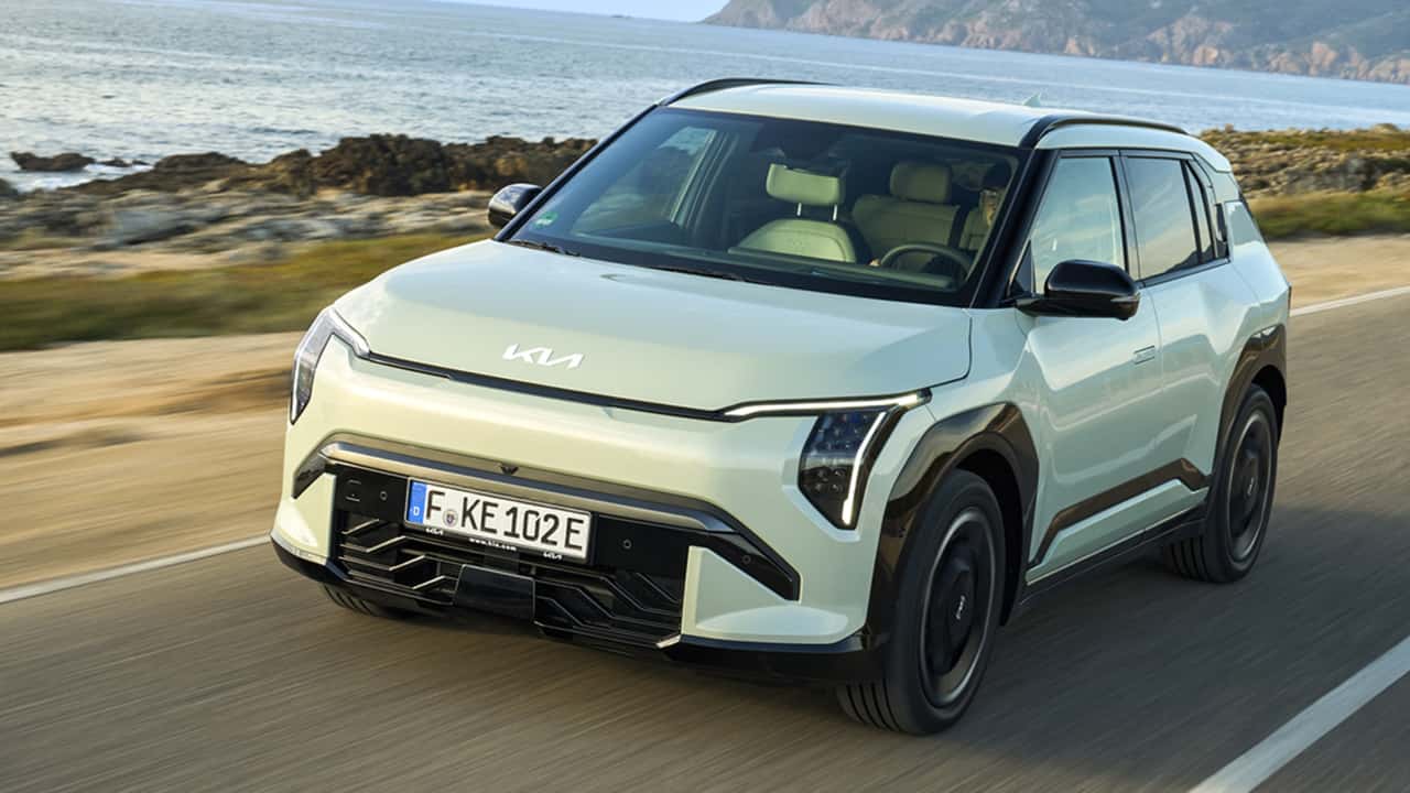 Une voiture électrique compacte et moderne de couleur bleue, garée près d'une borne de recharge en ville, symbolisant l'accessibilité croissante des véhicules électriques.