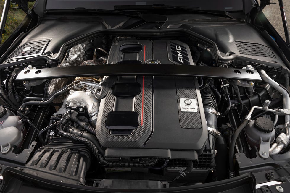 Vue détaillée du compartiment moteur d'une Mercedes-AMG C 63 S E PERFORMANCE, montrant le moteur hybride avec ses câbles et composants complexes, et le logo AMG.