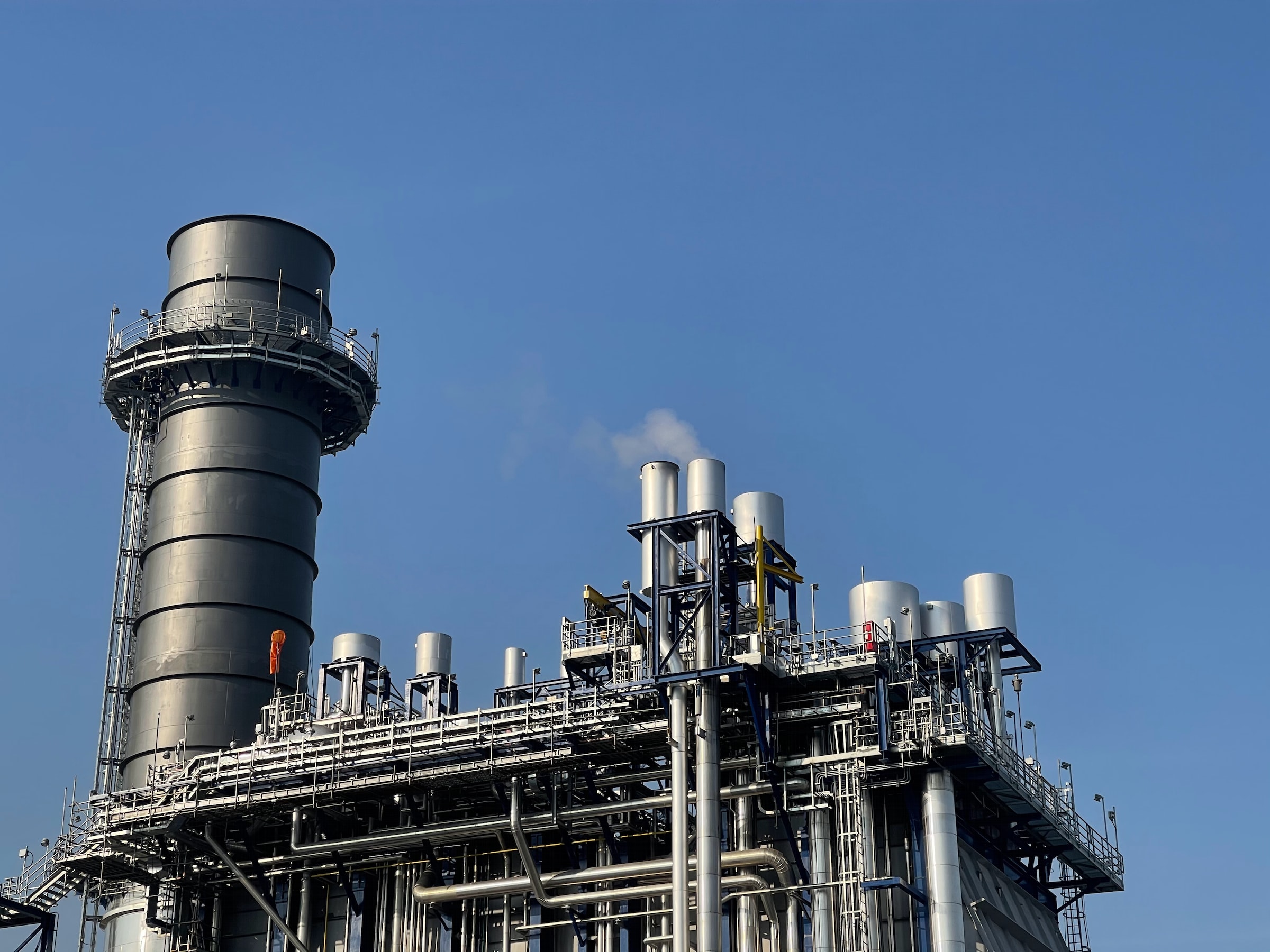 Vue aérienne d'une usine moderne de production d'e-fuels avec des éoliennes en arrière-plan.