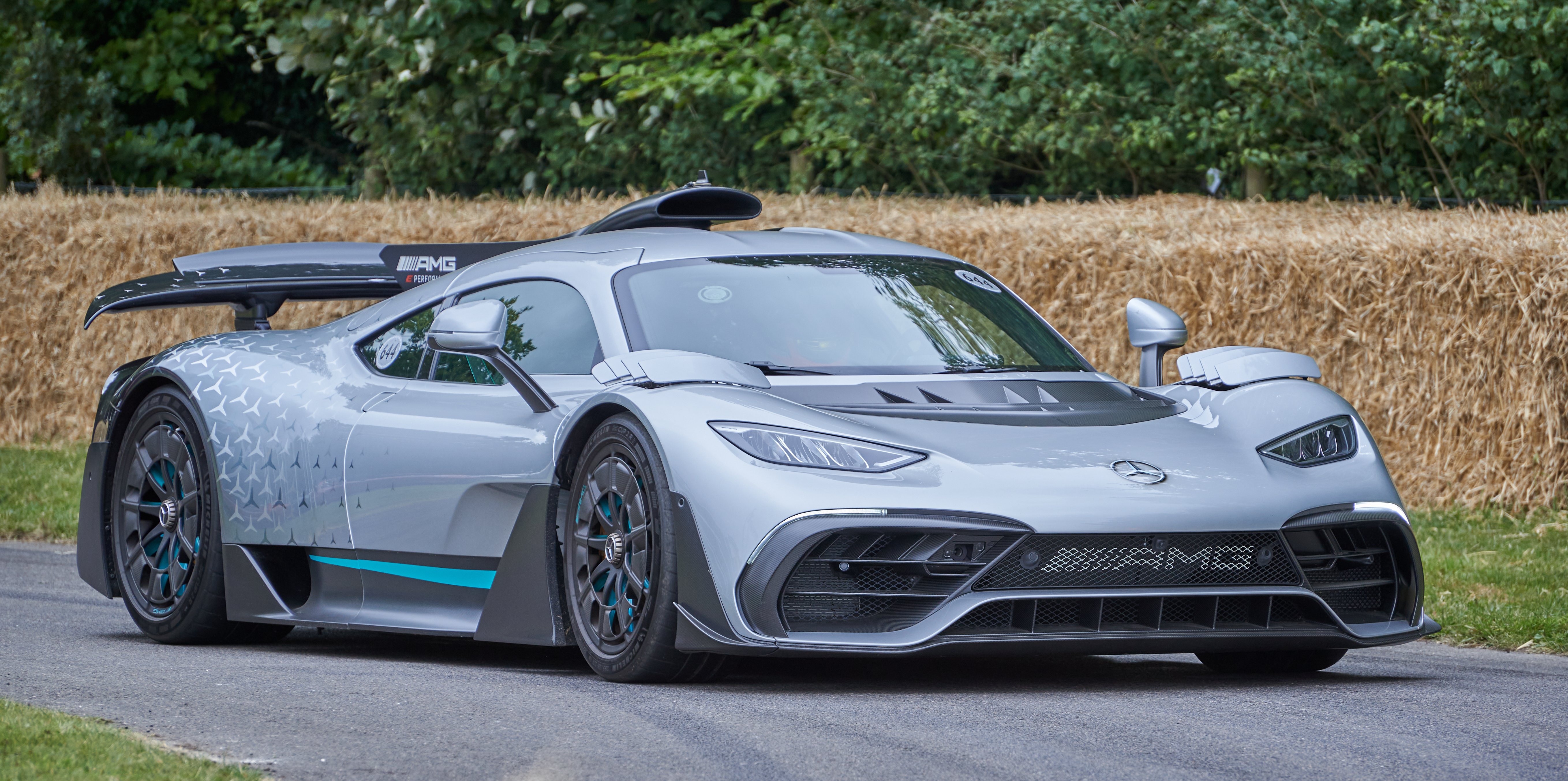 Vue latérale d'une AMG One argentée en pleine accélération sur un circuit de course, avec des traînées de vitesse floues en arrière-plan.