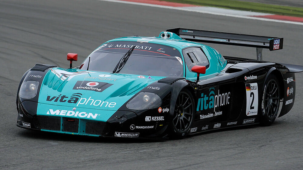 Une Maserati MC12 de course, bleue et blanche, en mouvement sur une piste.