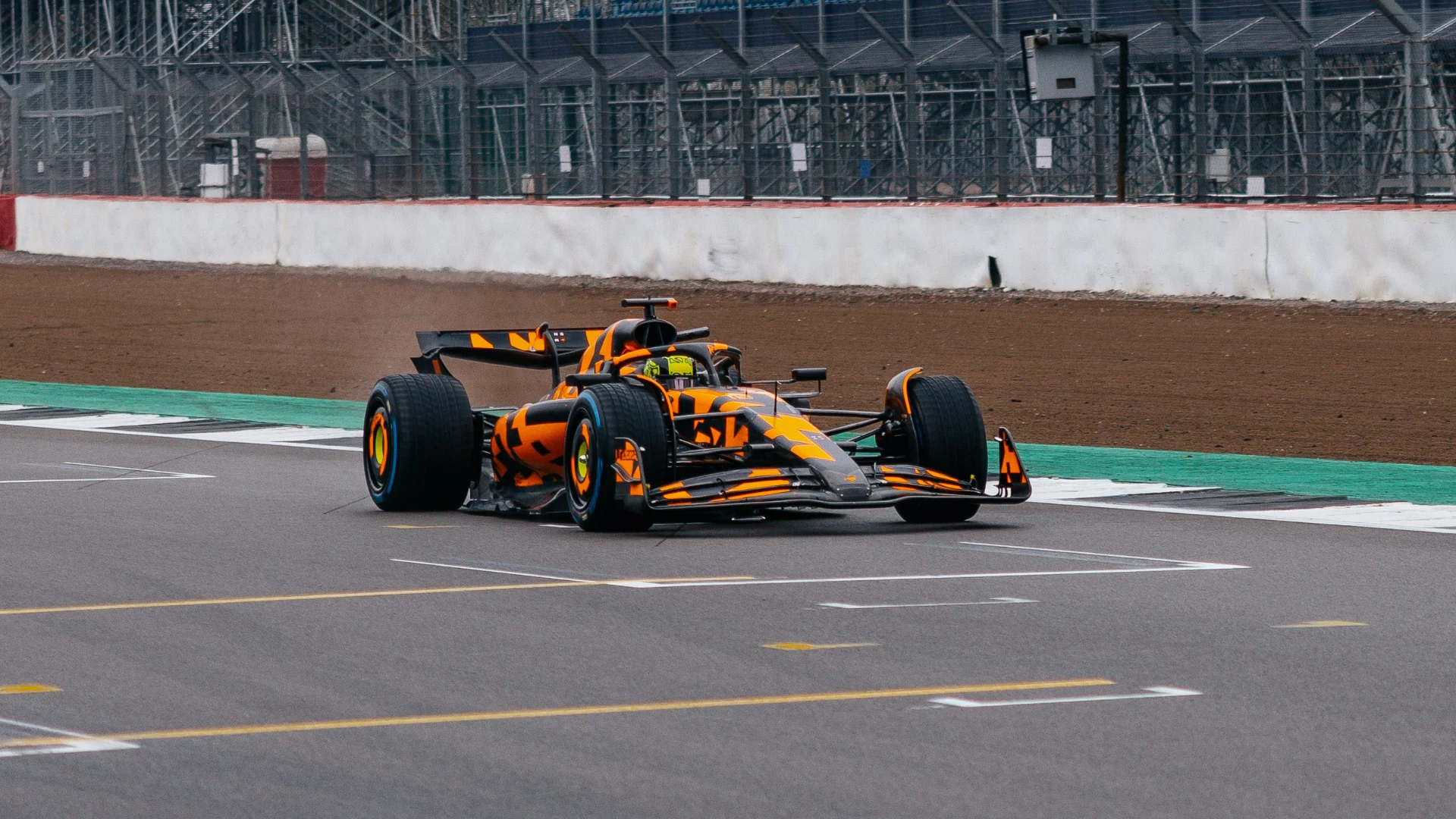 Une voiture de Formule 1 McLaren orange et noire en course sur une piste, avec un arrière-plan flou.