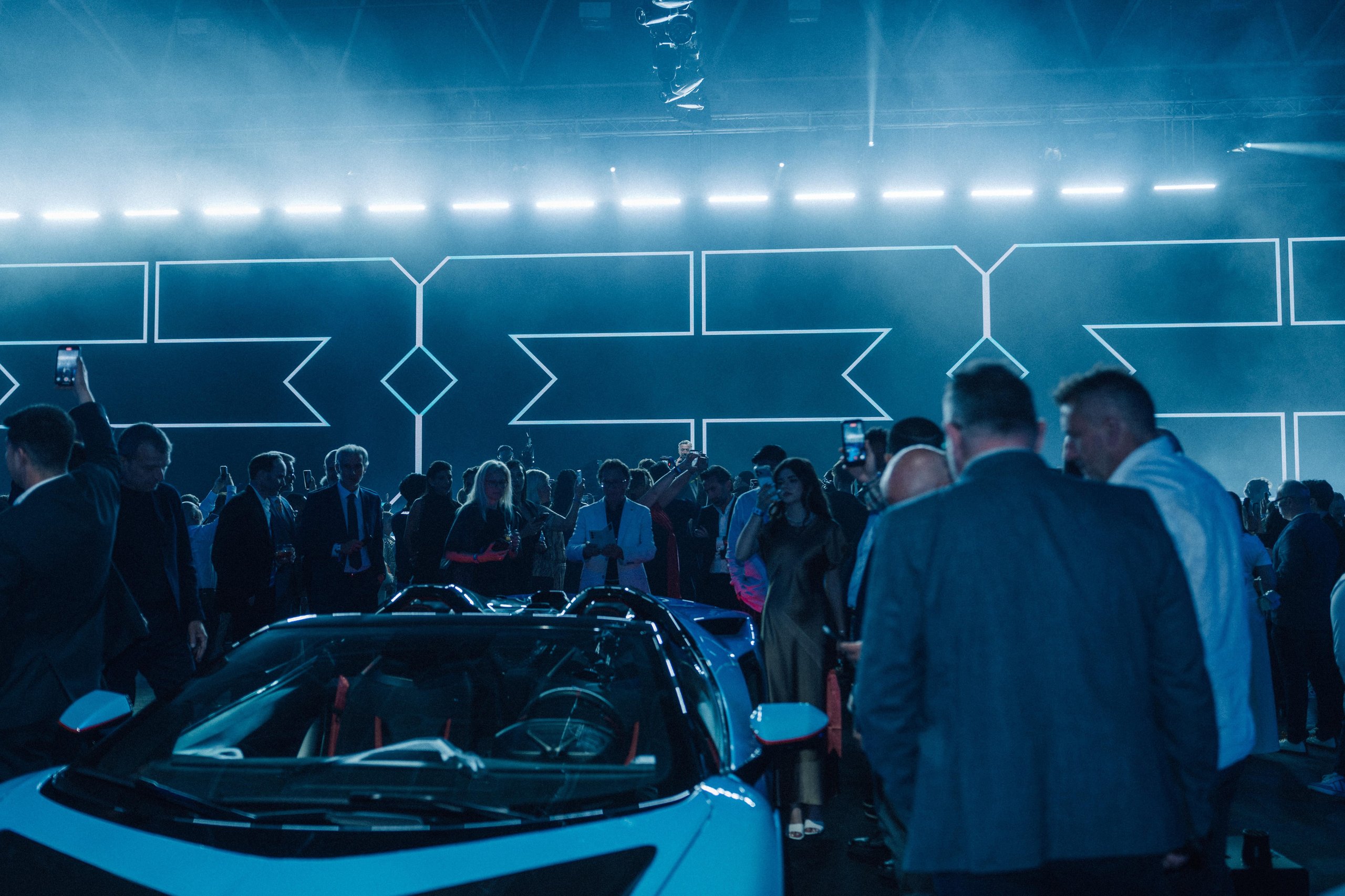 Des propriétaires d'hypercars se réunissant lors d'un événement officiel, avec plusieurs hypercars de luxe exposées dans un cadre élégant.