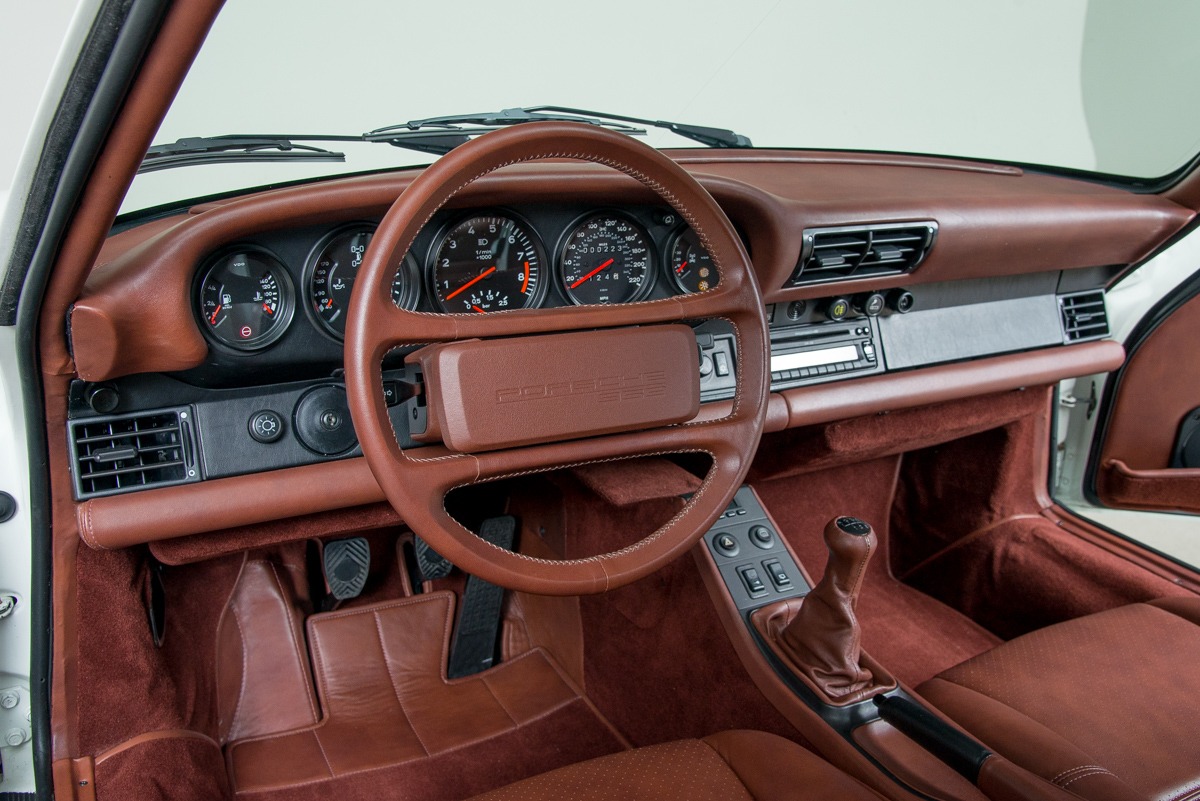 Intérieur de la Porsche 959 Komfort, présentant le tableau de bord, le volant et les sièges en cuir, soulignant le design classique et les matériaux de qualité.