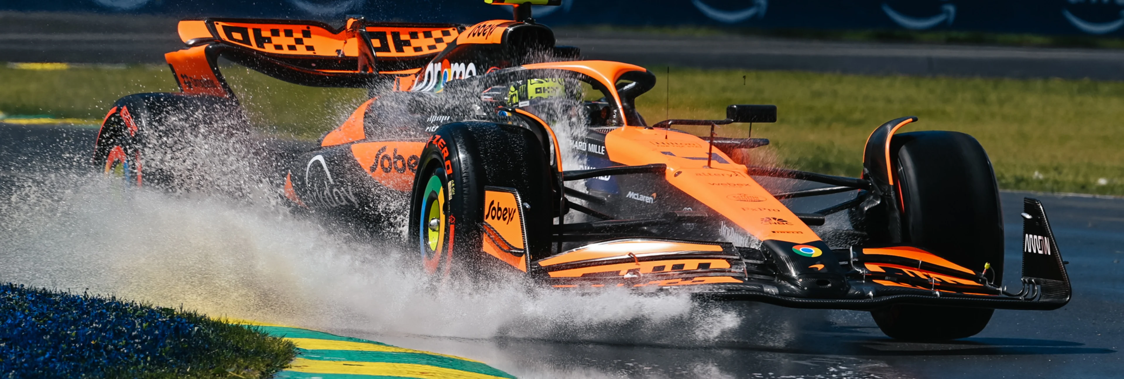 Une McLaren de Formule 1 orange et noire en virage sur le Circuit Gilles-Villeneuve, avec le fleuve Saint-Laurent ou la ville en arrière-plan.