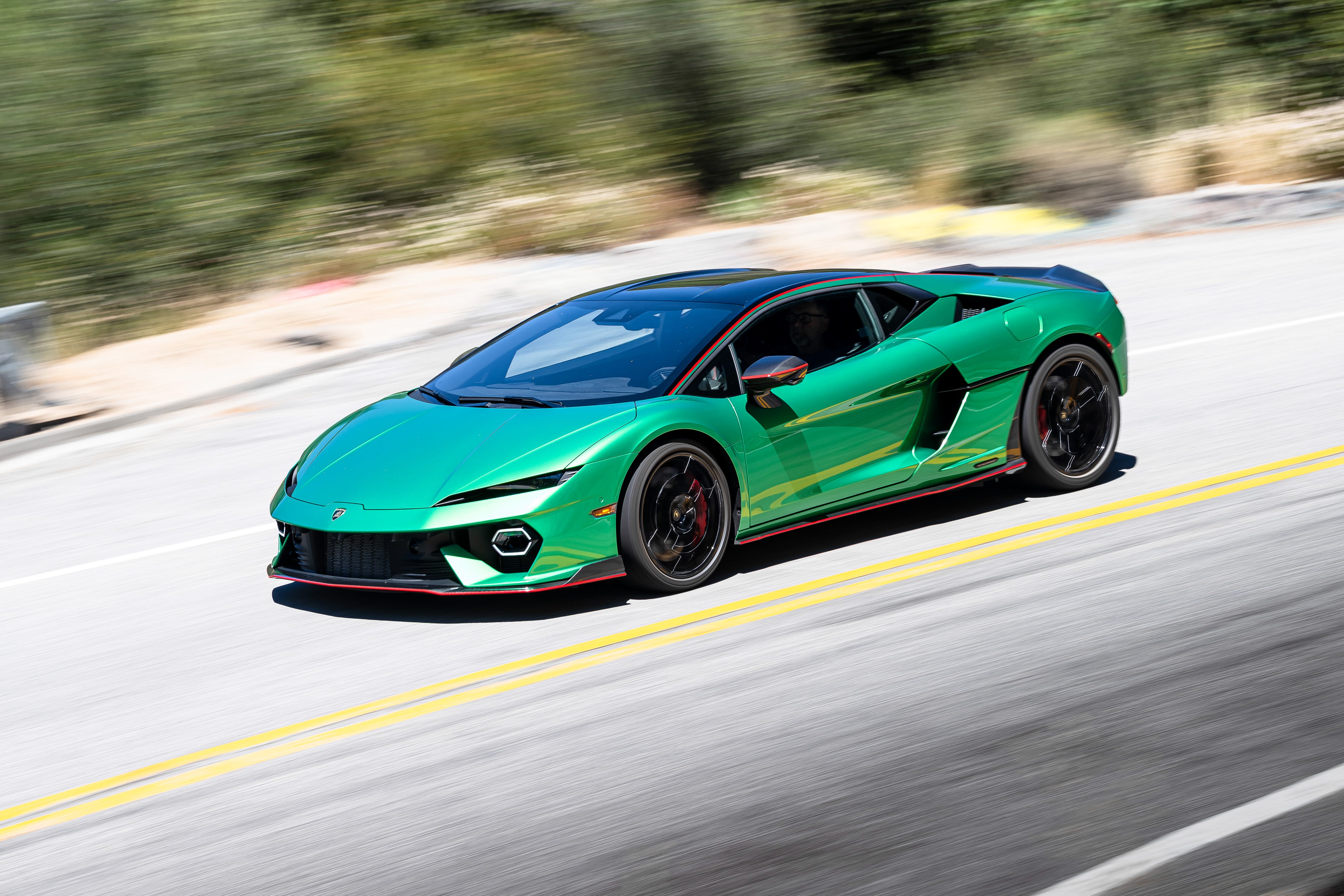 Une Lamborghini Temerario jaune, hypercar hybride, roulant sur une route de montagne sinueuse, mettant en valeur son design anguleux et ses feux arrière distinctifs.