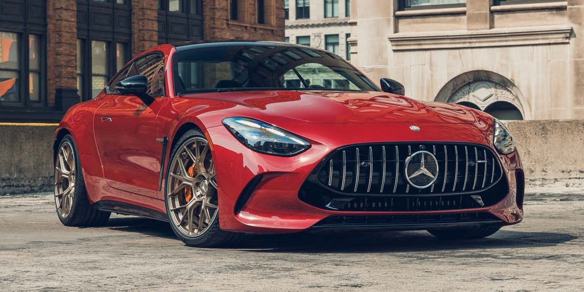 Vue latérale d'une Mercedes-AMG GT 2026 rouge foncé, en mouvement sur une route de campagne sinueuse, mettant en valeur son design sportif et ses lignes fluides.