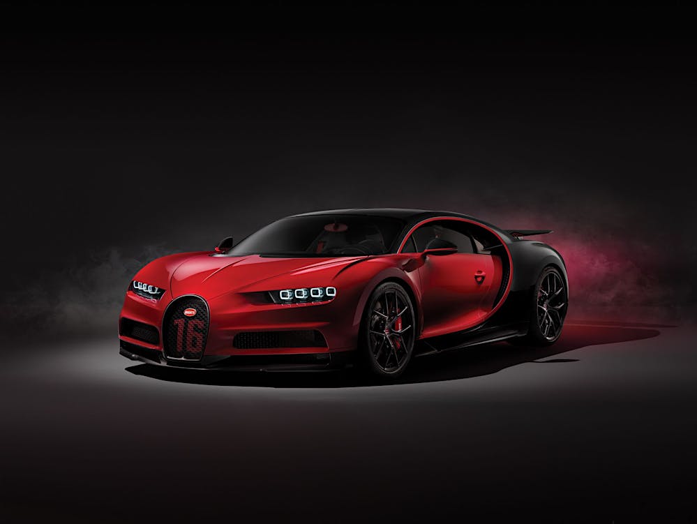 Une Bugatti Chiron Super Sport 300+ orange et noire en mouvement rapide sur une piste, avec le lac Léman et des montagnes en arrière-plan.