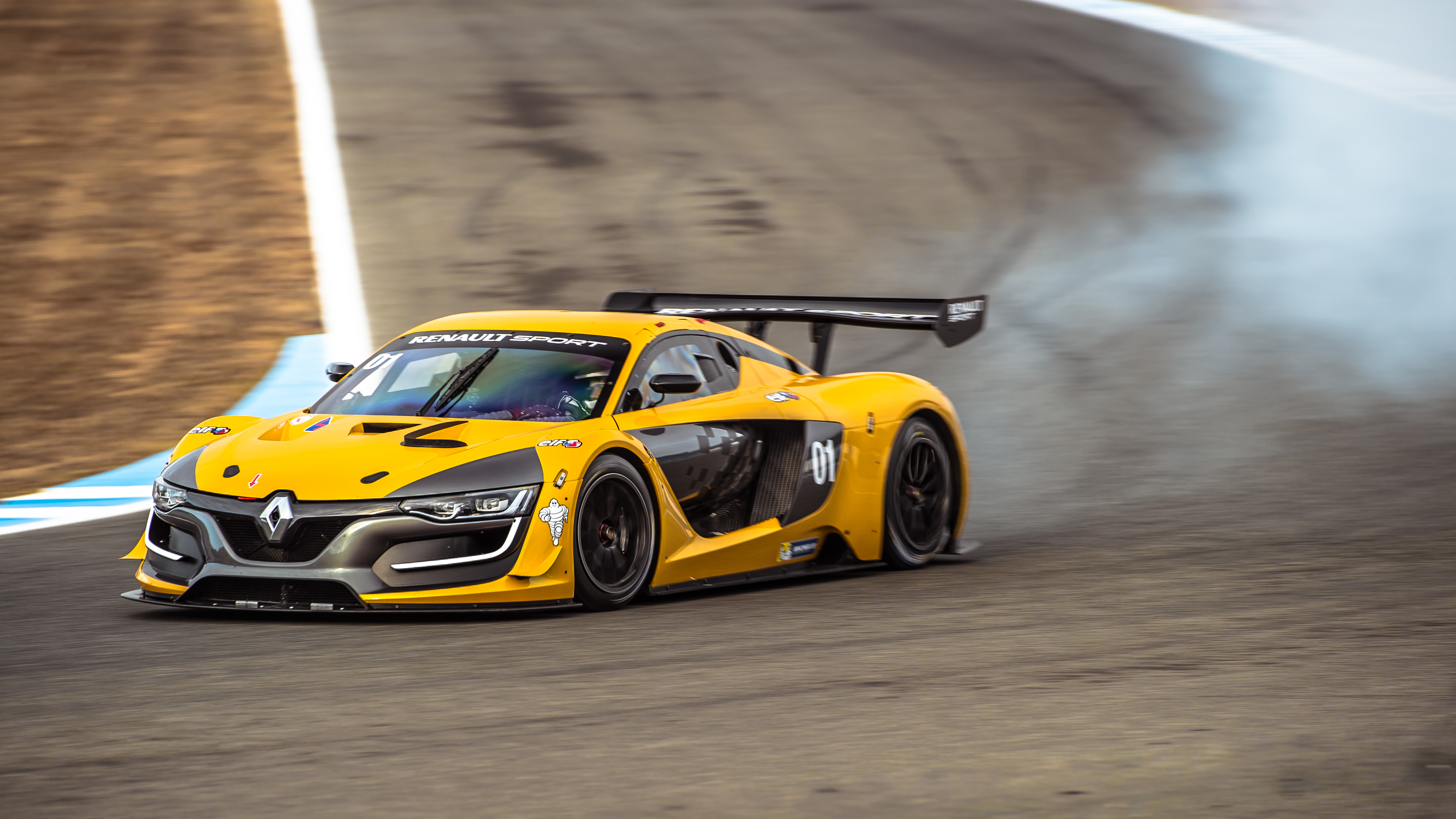 Une Renault Sport R.S. 01 jaune et noire en pleine course sur une piste, avec des pneus fumants et une grande vitesse.