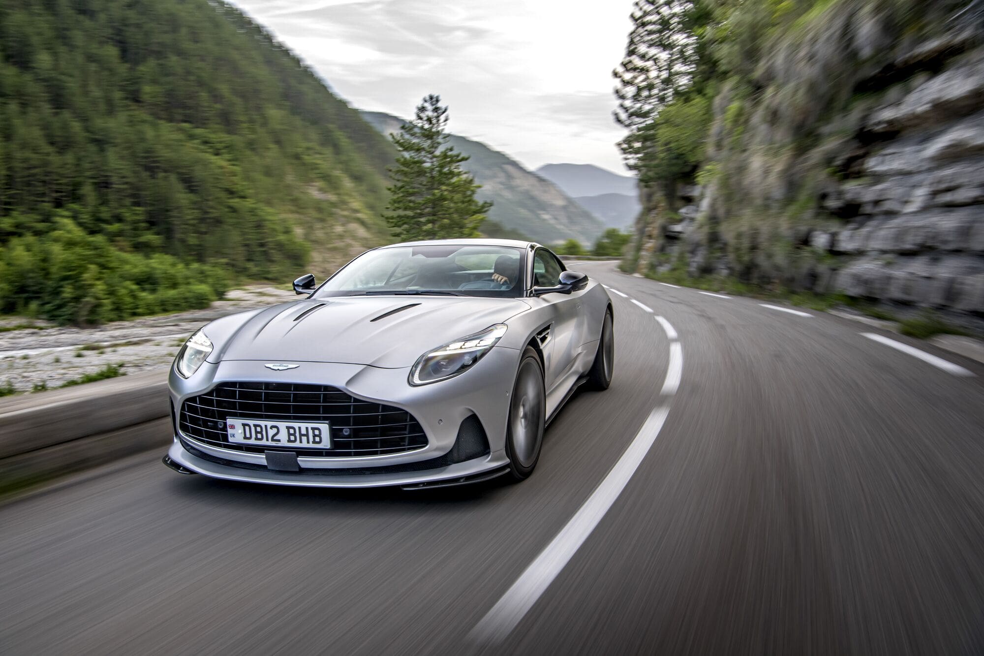 Une Aston Martin DB12 grise avec des pneus hiver, avançant avec précaution sur une route couverte de glace et de neige.