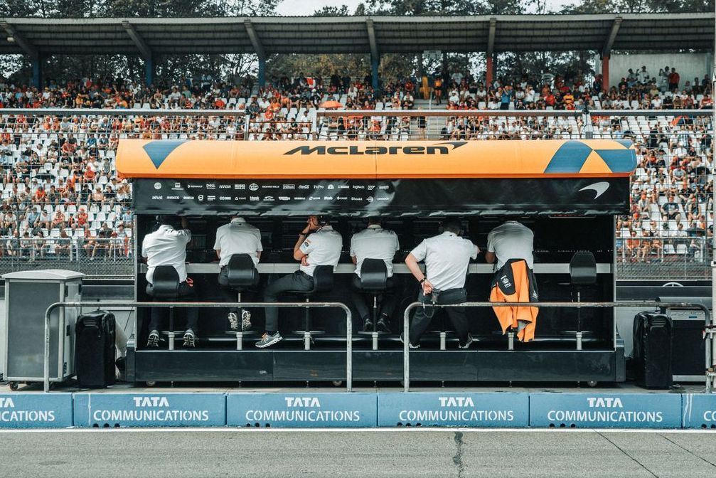 Des membres de l'équipe de stratégie McLaren sur le muret des stands, observant des écrans de données pendant une course de Formule 1.