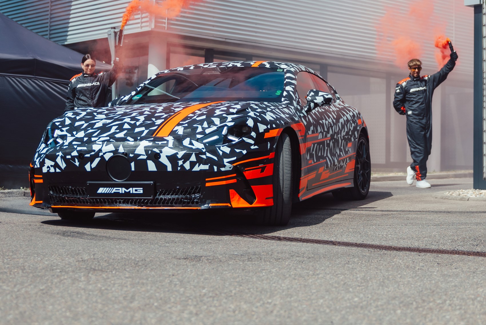 Vue latérale d'une Mercedes-AMG GT Coupé 4 portes électrique de couleur sombre, en mouvement sur une piste d'essai, avec des reflets bleus subtils.