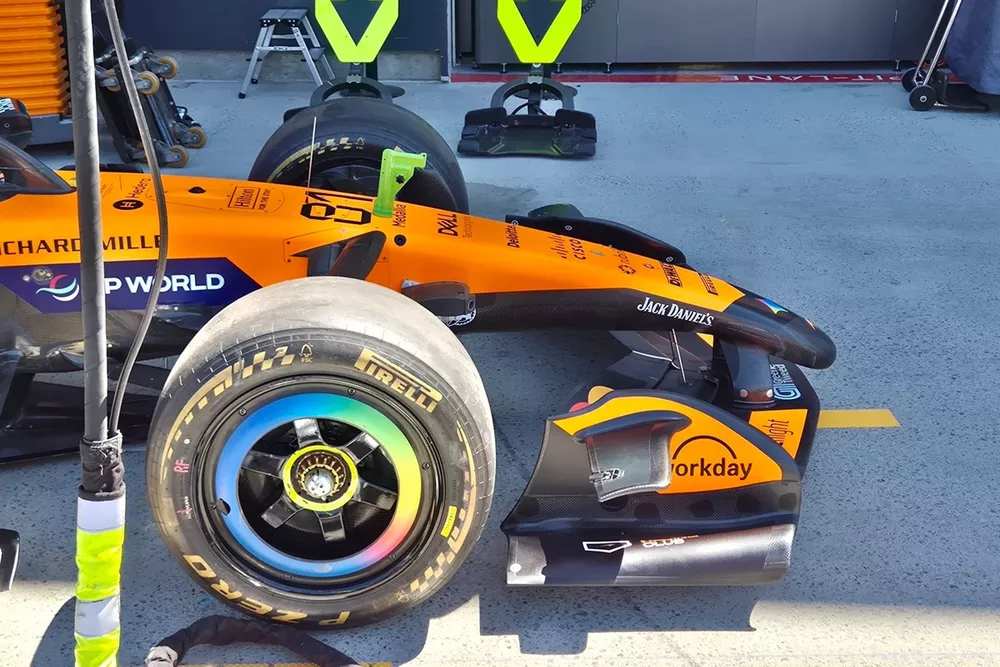 Gros plan détaillé de l'aileron avant d'une voiture de Formule 1 McLaren, montrant les éléments aérodynamiques complexes et la texture en fibre de carbone.