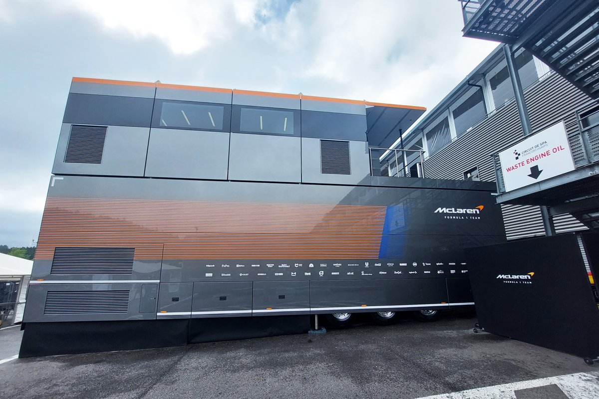Vue du paddock de l'équipe McLaren de Formule 1, avec des mécaniciens et ingénieurs s'affairant autour d'une voiture de course.