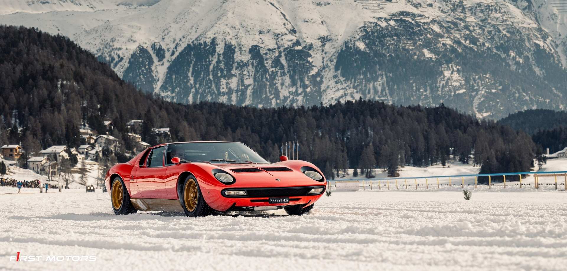 Une supercar rouge ou jaune roulant sur une route de montagne enneigée, avec des sommets alpins en arrière-plan sous un ciel clair.