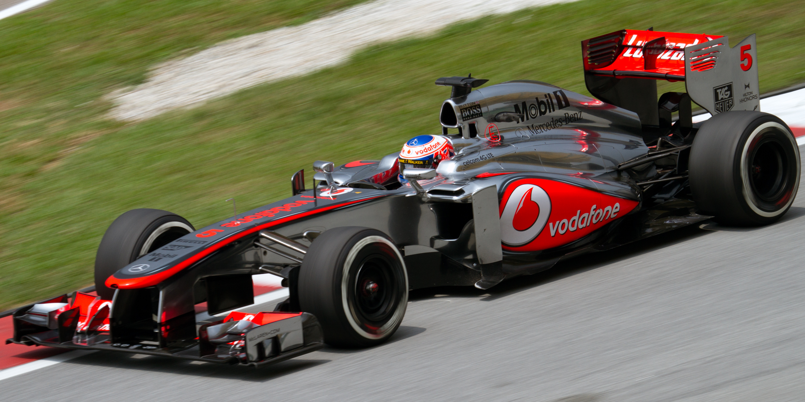 Une voiture de Formule 1 McLaren moderne avec un moteur V8 visible, en mouvement sur une piste de course.