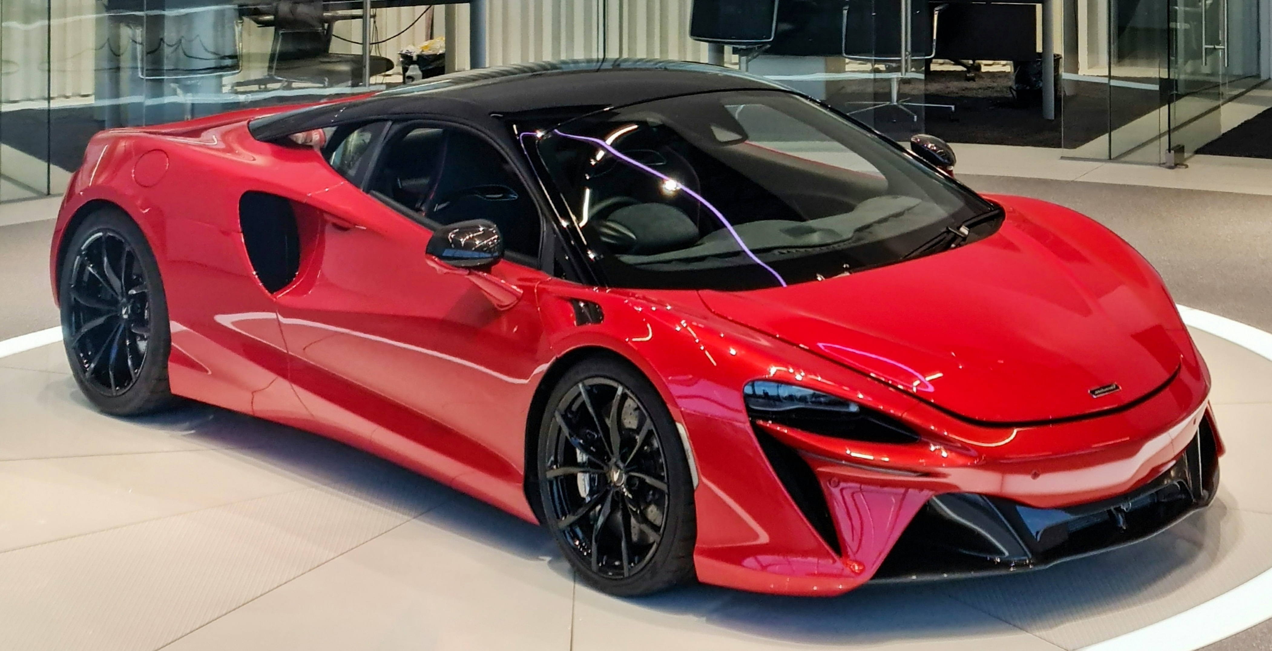 Une McLaren Artura de couleur vive, en mouvement sur une route sinueuse, avec un arrière-plan flou de paysage.