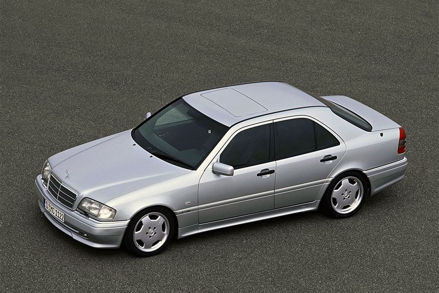 Une Mercedes-AMG C36 AMG W202 argentée, classique et élégante, garée dans une rue pavée.