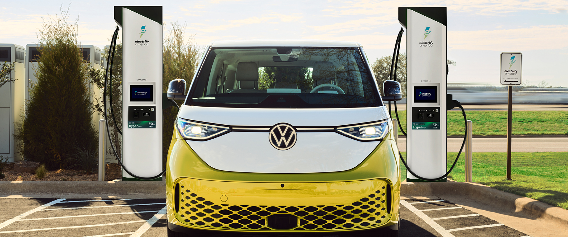 Une voiture électrique Volkswagen branchée à une station de recharge rapide, avec des lumières urbaines en arrière-plan.