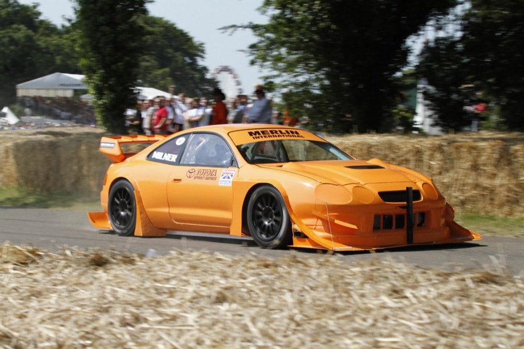 Une Toyota Celica fortement modifiée avec un kit carrosserie large, une suspension abaissée et une peinture personnalisée, garée sur le circuit du Nogaro Motor Festival.