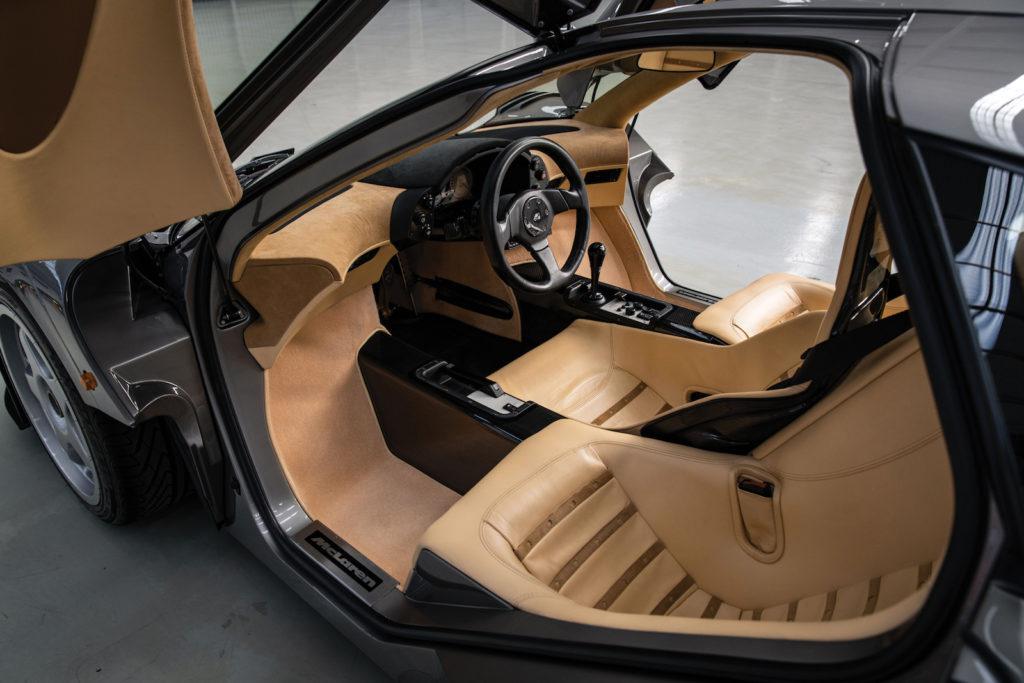 Vue de l'intérieur de la McLaren F1, montrant le siège du conducteur au centre et les deux sièges passagers.