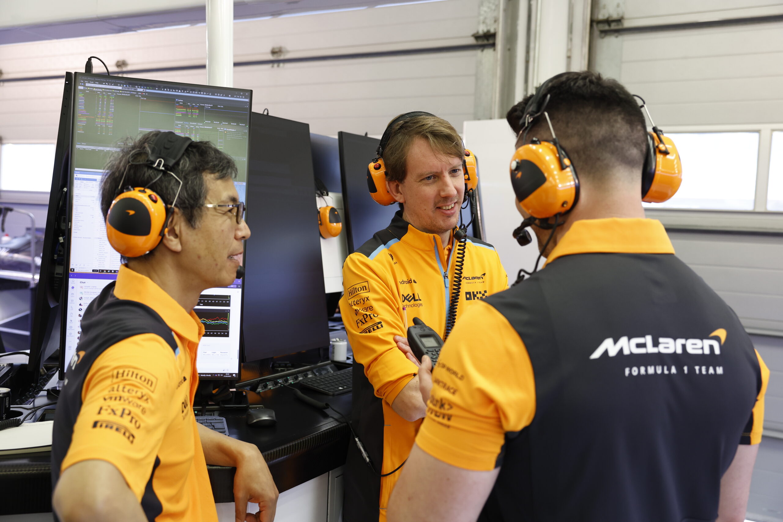 Des ingénieurs de l'équipe McLaren F1 concentrés devant des écrans d'ordinateur affichant des graphiques et des données techniques.