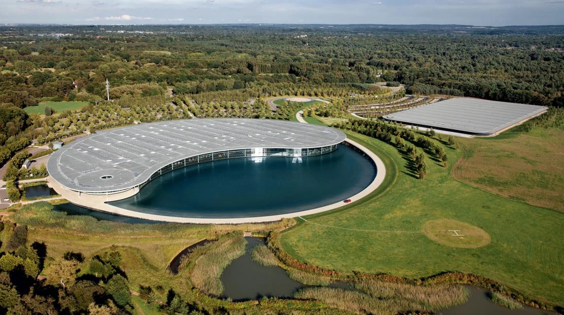 Vue aérienne du McLaren Technology Centre à Woking, un bâtiment futuriste entouré d'un lac et de verdure.