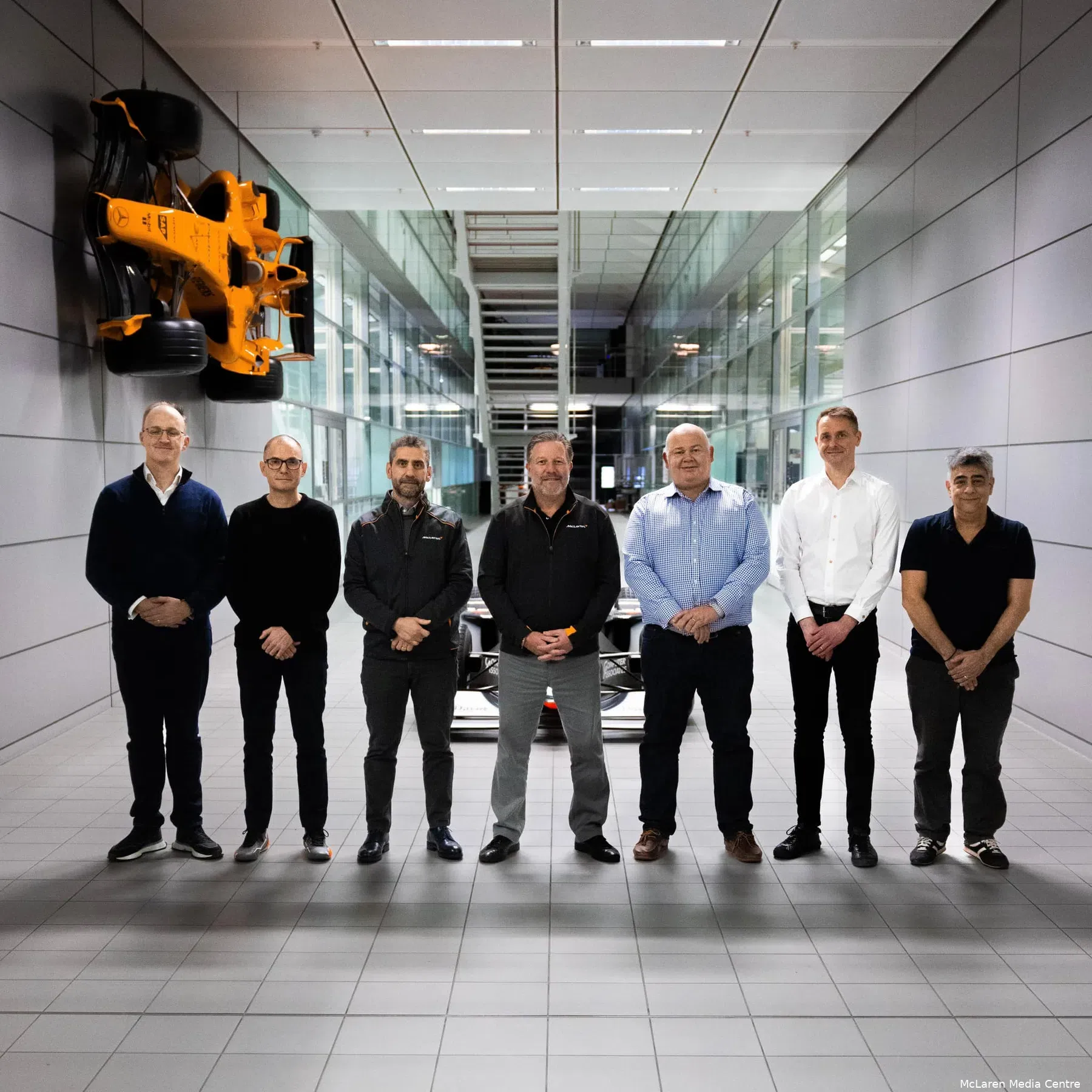 Des ingénieurs de l'équipe McLaren F1 en pleine discussion devant des écrans d'ordinateur affichant des données techniques, dans un bureau moderne et lumineux.