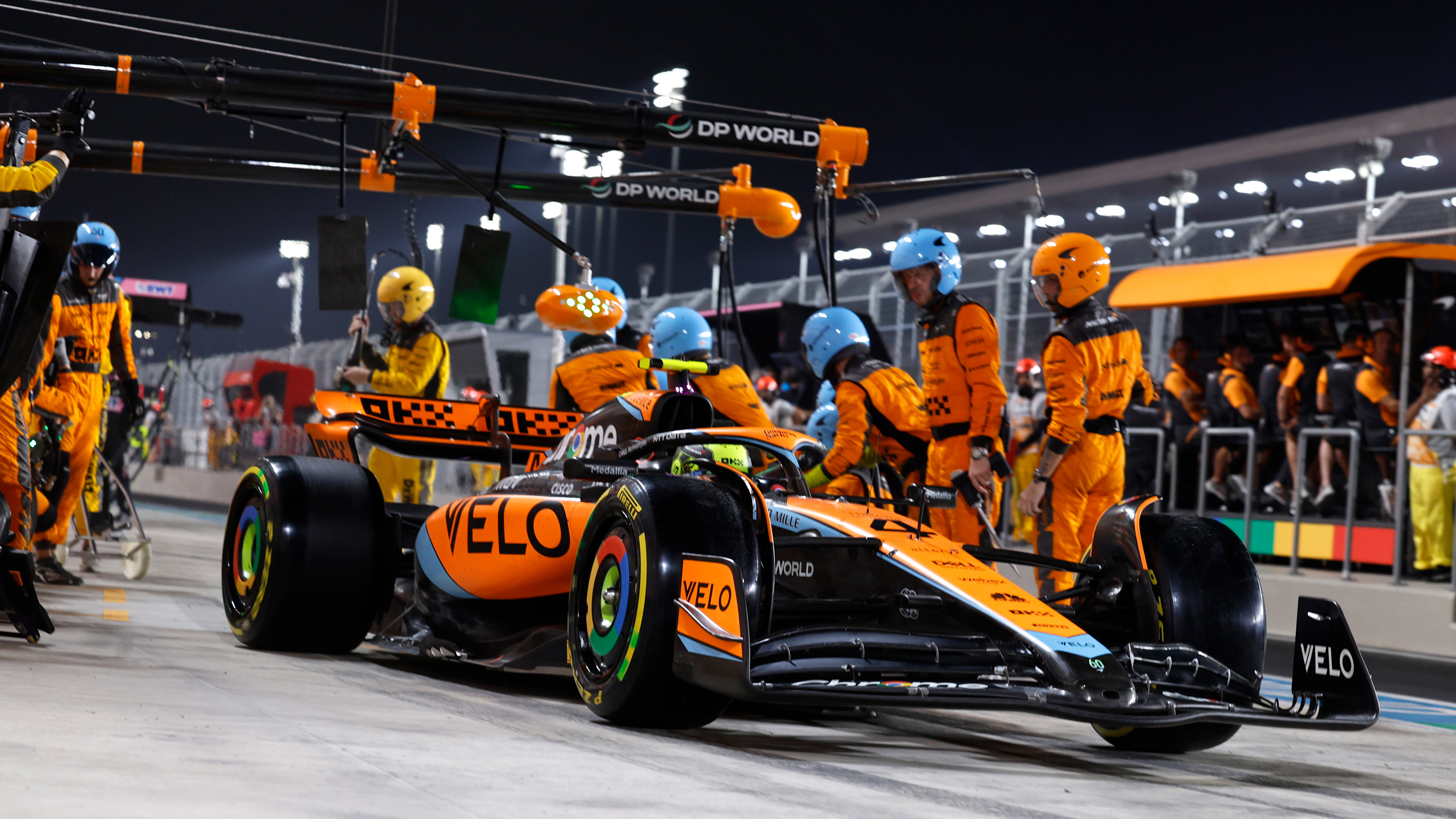 Photo dynamique d'une voiture de Formule 1 McLaren lors d'un arrêt au stand, avec l'équipe de mécaniciens travaillant rapidement et de manière coordonnée.