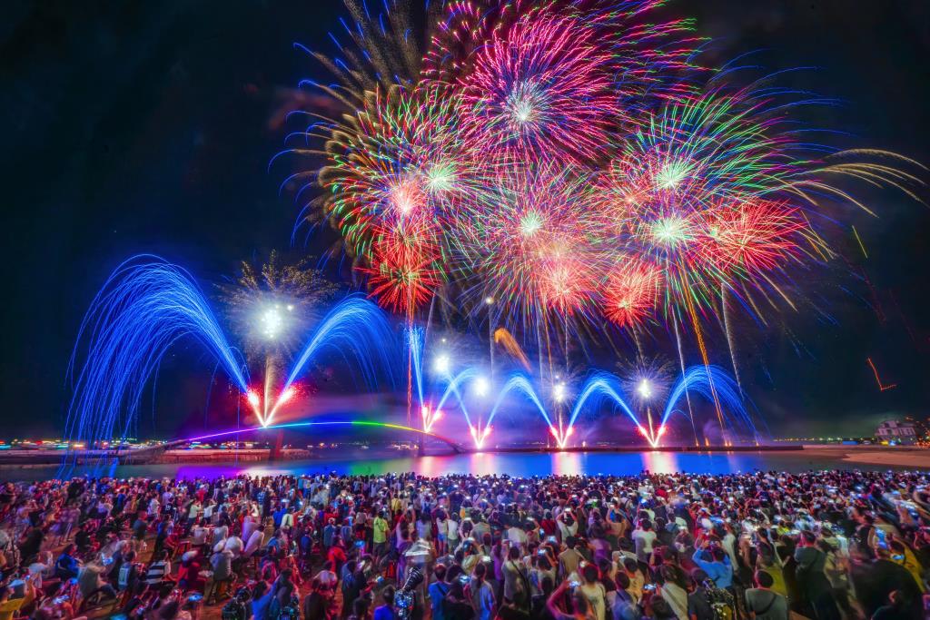 Un feu d'artifice éclatant au-dessus de plusieurs supercars garées sur une plage la nuit à Penghu.