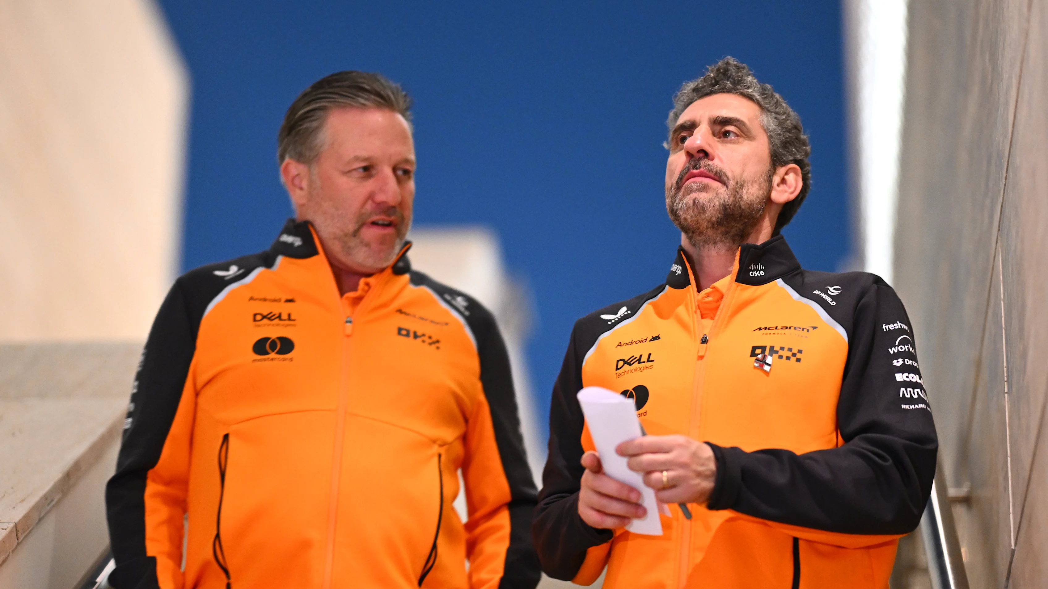 Andrea Stella et Zak Brown, en tenue McLaren, dans le garage de l'équipe, examinant des écrans de données.