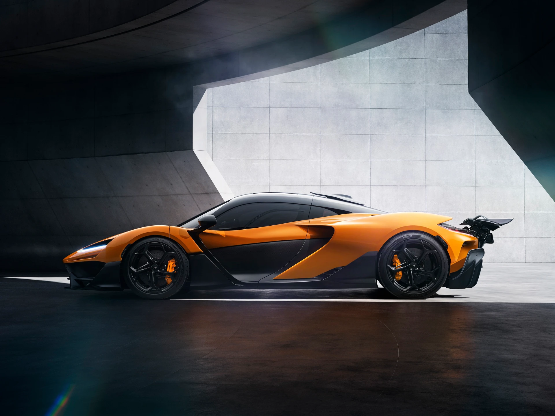 Vue latérale d'une McLaren W1 rouge vif sur une piste de course, mettant en évidence ses lignes aérodynamiques, ses prises d'air et son diffuseur arrière.