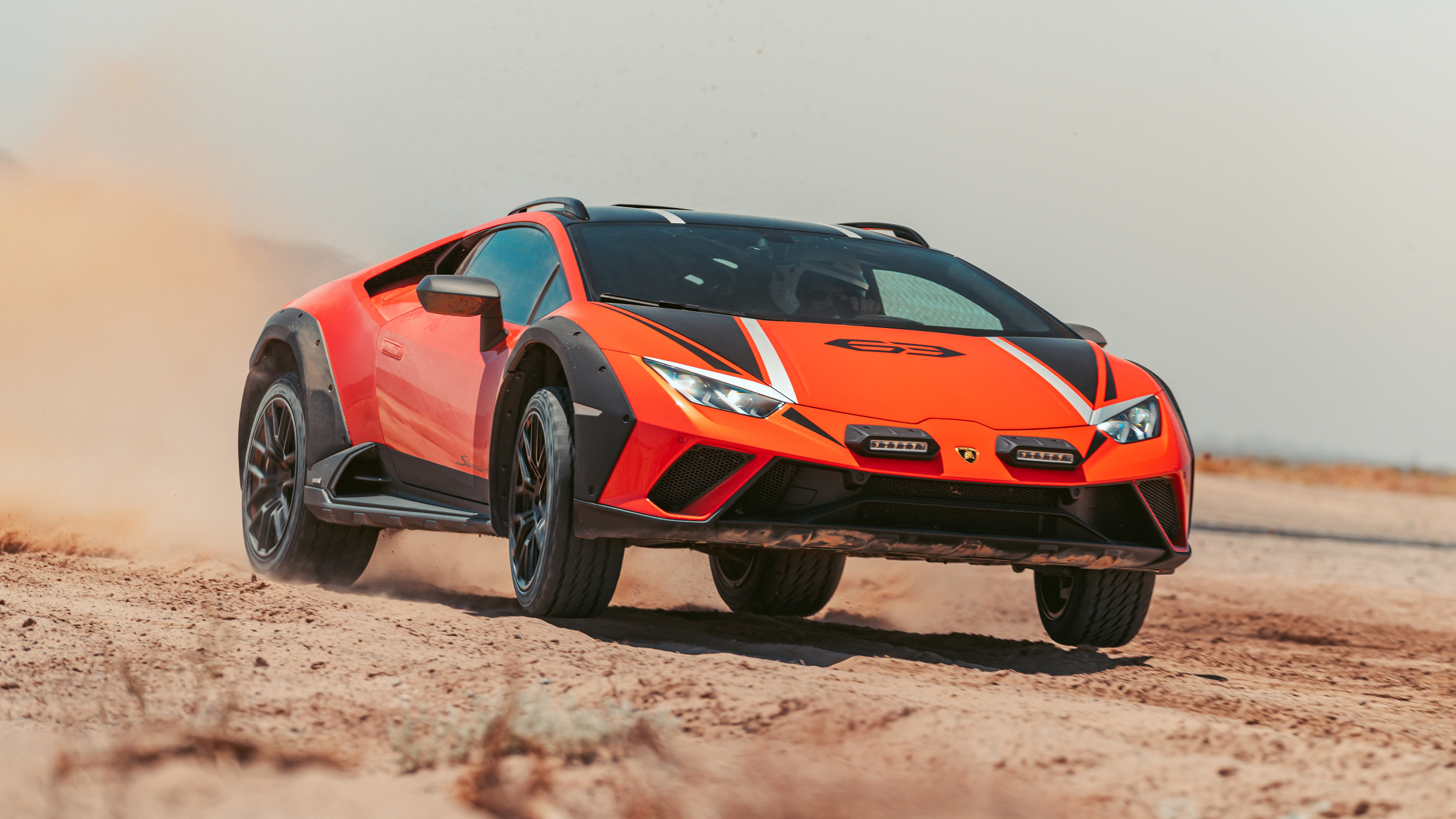 Une Lamborghini Huracán Sterrato roulant sur une route de gravier, soulevant de la poussière, mettant en évidence son design agressif et ses capacités hors route.
