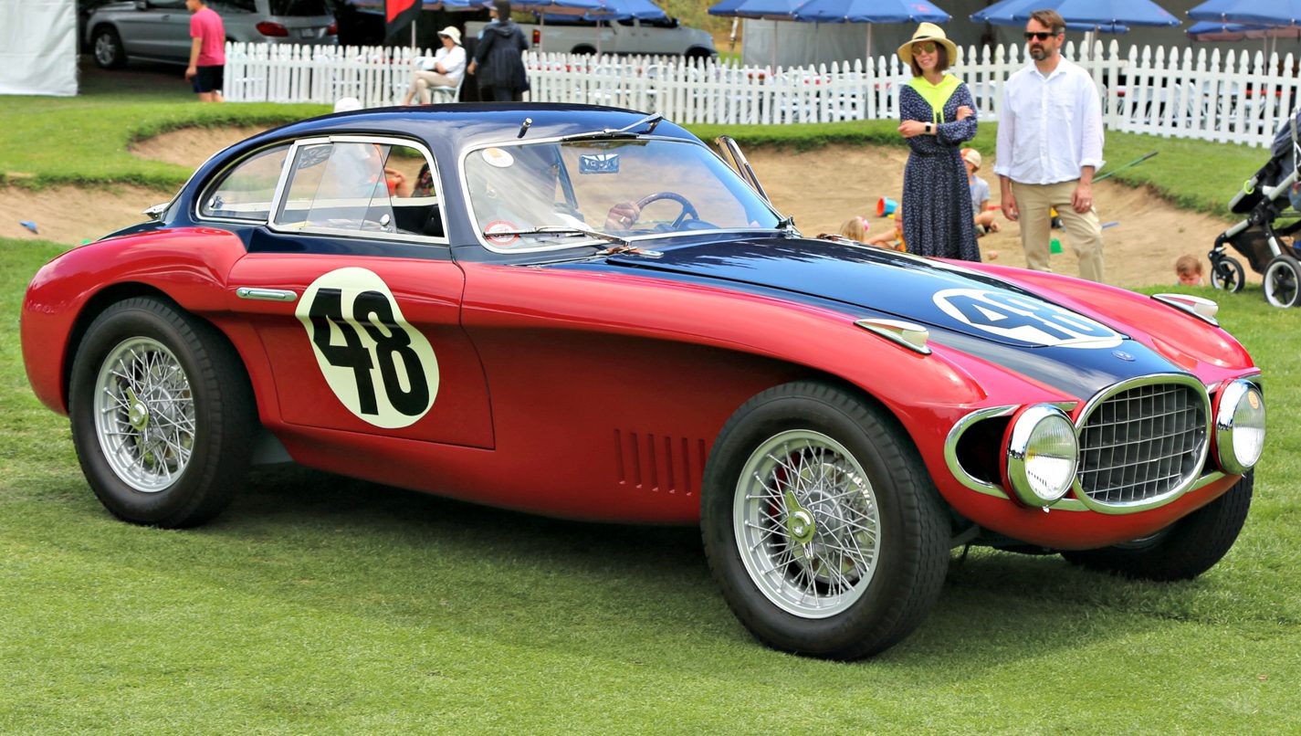 Image d'une Ferrari 250 GT rouge classique, garée sur l'herbe, avec des spectateurs en arrière-plan lors du Concours d'Élégance de Hillsborough.