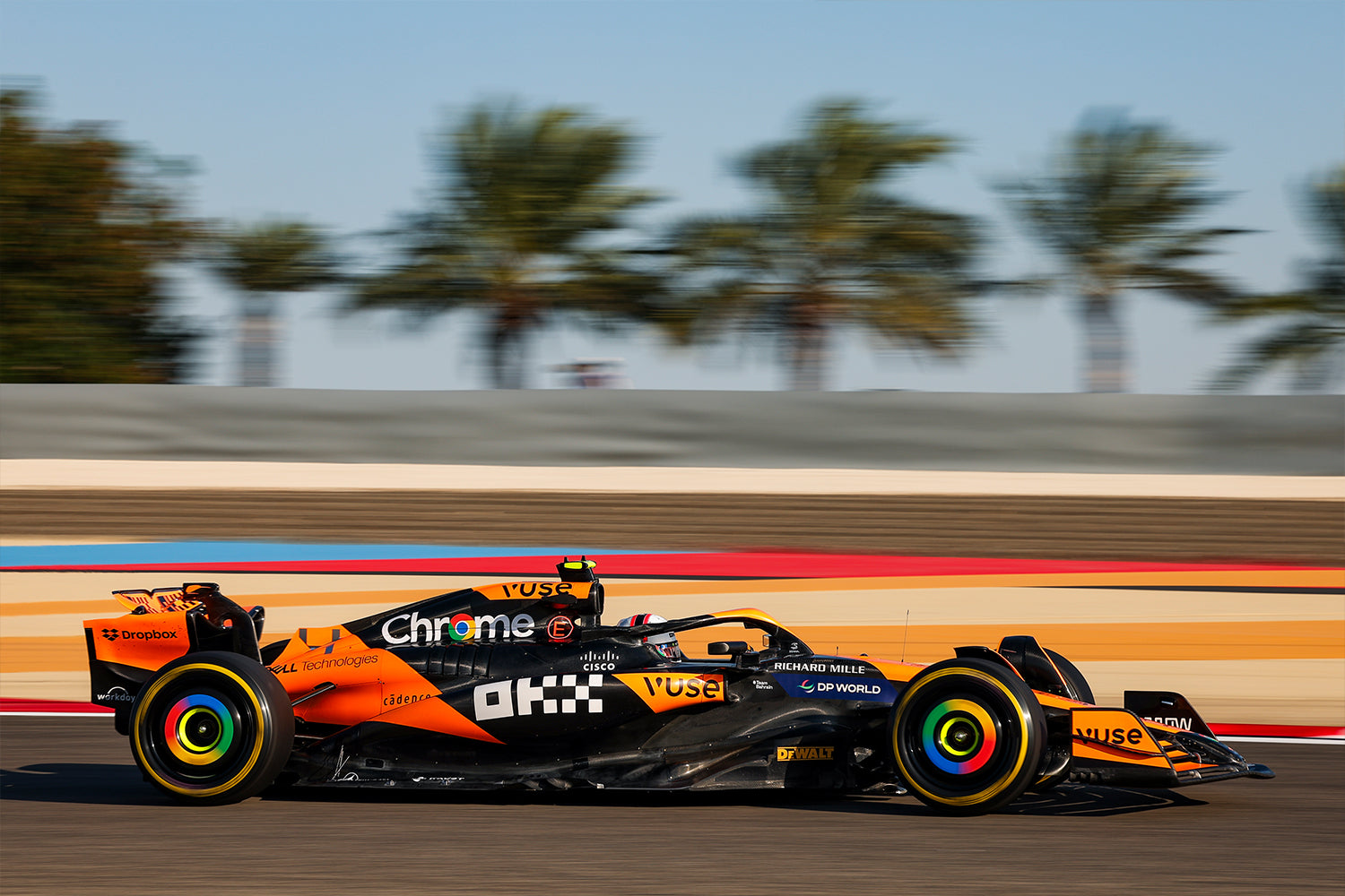 Une voiture de Formule 1 McLaren MCL38 orange et noire en pleine course sur un circuit, vue de côté, avec un arrière-plan flou.
