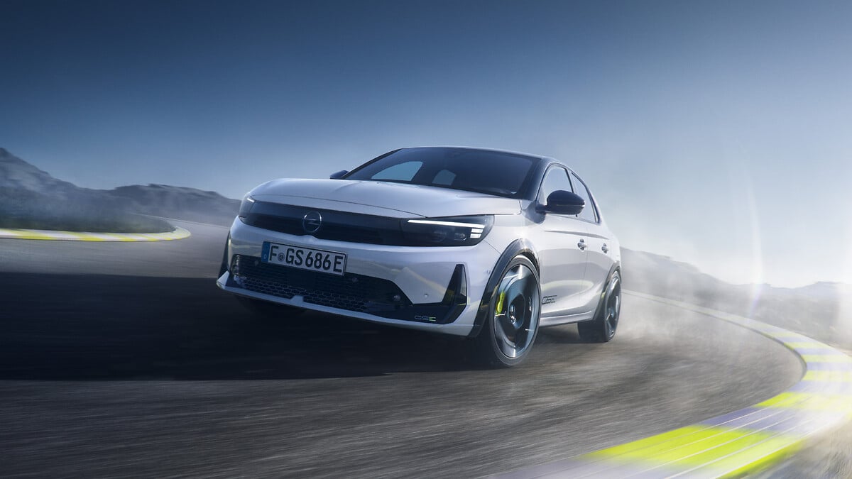 Une Opel Corsa GSE bleue, une voiture de sport électrique, en mouvement sur une route sinueuse, vue de côté et légèrement de l'arrière, mettant en valeur son design dynamique et ses jantes sportives.