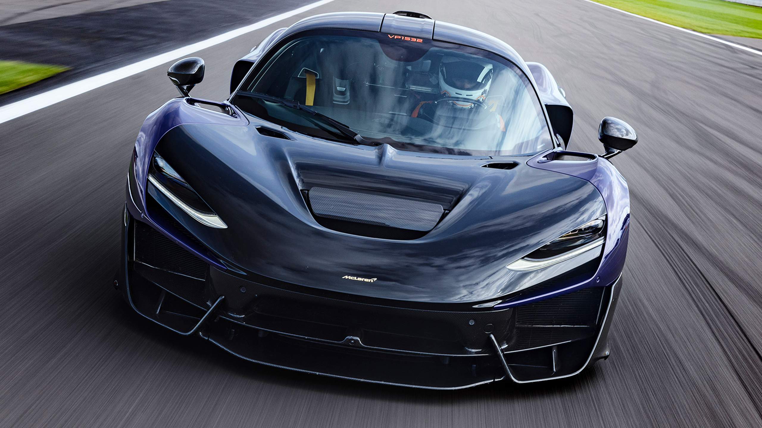 Image d'un prototype de la McLaren W1 camouflé, roulant à grande vitesse sur le circuit de Silverstone, avec un aileron arrière proéminent.
