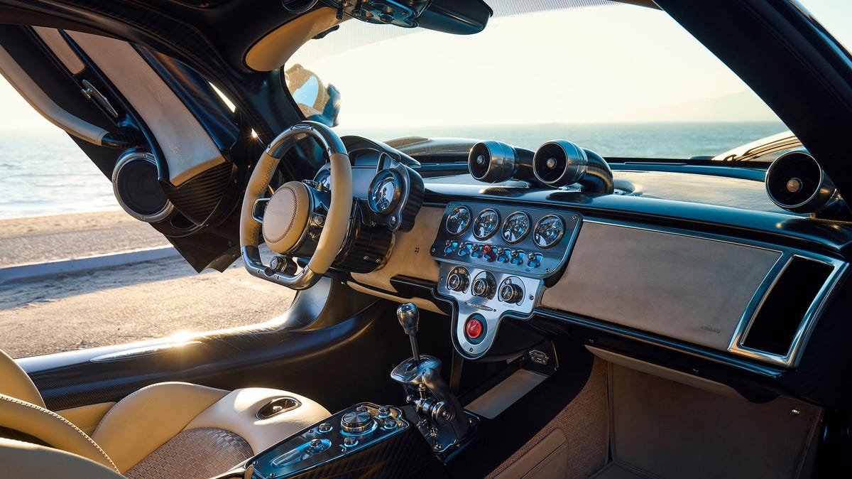 Une Pagani Utopia grise, vue de côté, roulant sur une route sinueuse avec un coucher de soleil en arrière-plan.