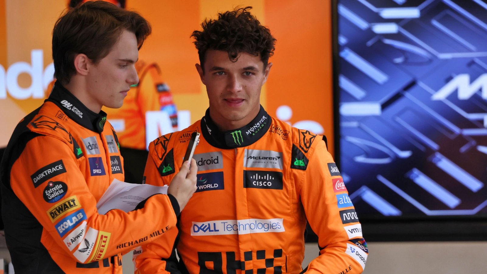 Lando Norris et Oscar Piastri, pilotes McLaren, discutant avec des ingénieurs dans le garage de Formule 1.