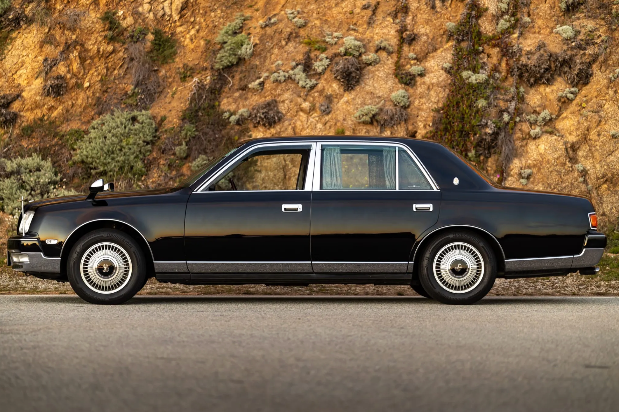 Une Toyota Century V12 noire de 1997, garée de nuit dans une rue de Tokyo, ses lignes élégantes reflétant les néons de la ville.