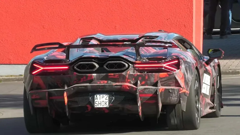 Vue arrière d'un prototype Lamborghini Revuelto SVJ gris foncé sur le circuit du Nürburgring, avec un aileron arrière imposant et des éléments aérodynamiques proéminents.