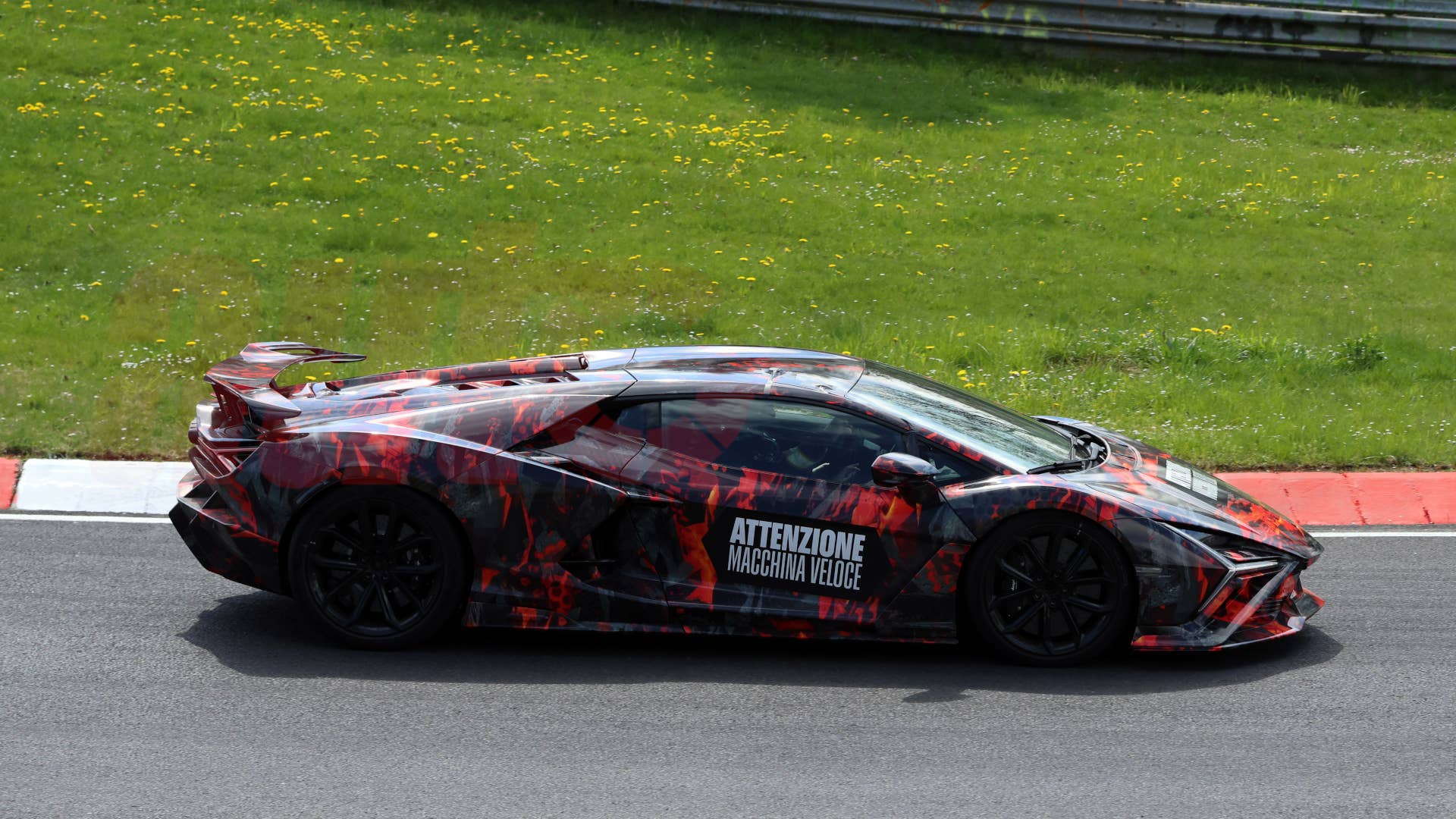 Profil latéral d'un prototype Lamborghini Revuelto SVJ gris foncé en pleine courbe sur le Nürburgring, avec des jupes latérales proéminentes et des prises d'air agrandies.