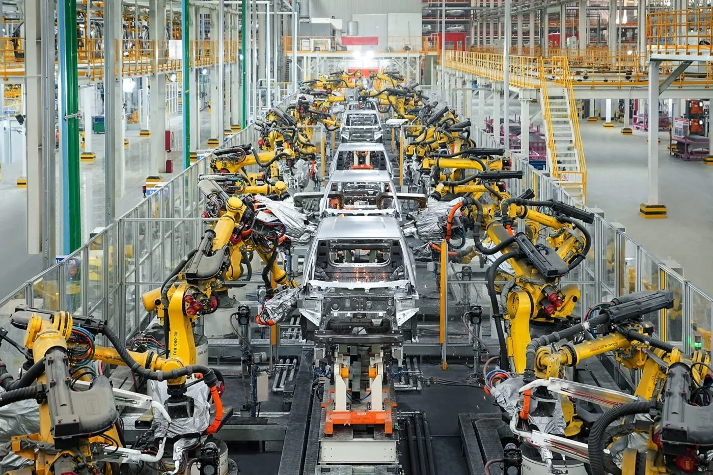 Vue intérieure d'une usine de voitures électriques BYD en Europe, montrant des robots et des ouvriers sur une chaîne de montage.