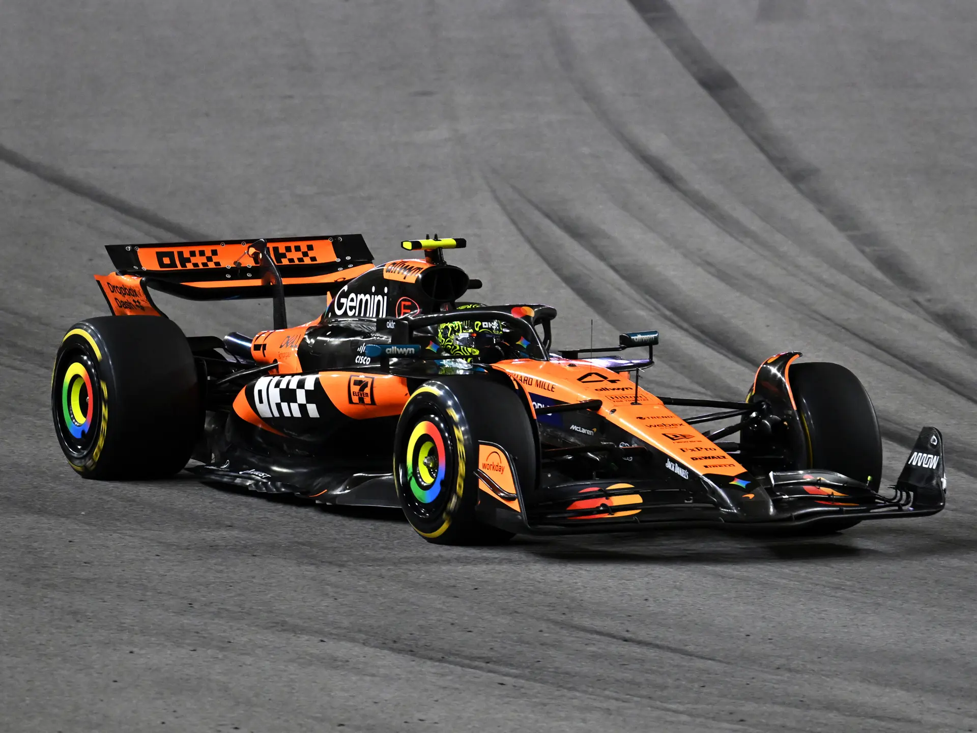 Une voiture de Formule 1 McLaren orange et noire, filant à toute vitesse sur une piste de course, avec un arrière-plan flou suggérant le mouvement.