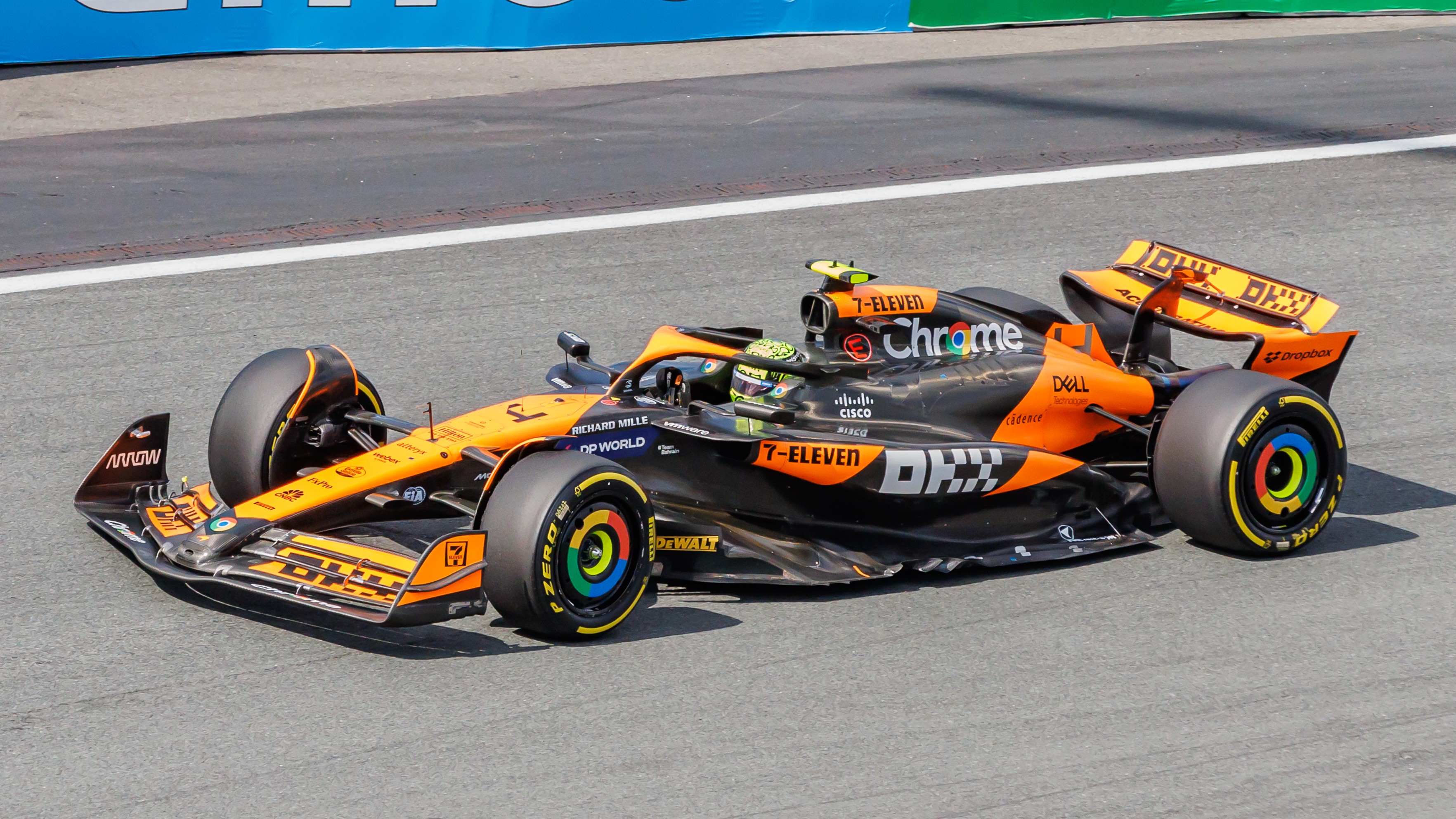 Une voiture de Formule 1 McLaren MCL38 orange et noire, pilotée par Lando Norris ou Oscar Piastri, en pleine course sur le circuit de Marina Bay à Singapour, avec les gratte-ciel illuminés en arrière-plan.