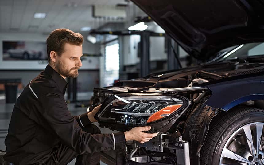 Un mécanicien professionnel travaillant sur une voiture Mercedes-Benz dans un atelier, utilisant des outils spécialisés.