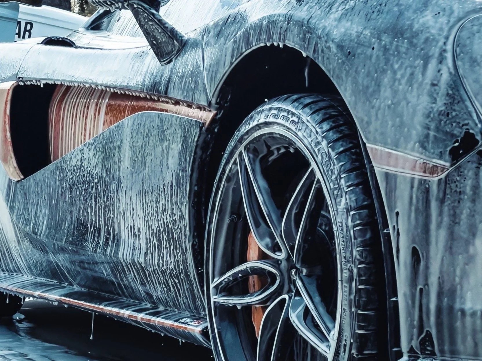 Un mécanicien nettoyant le dessous d'une supercar sur un pont élévateur, illustrant l'entretien hivernal.