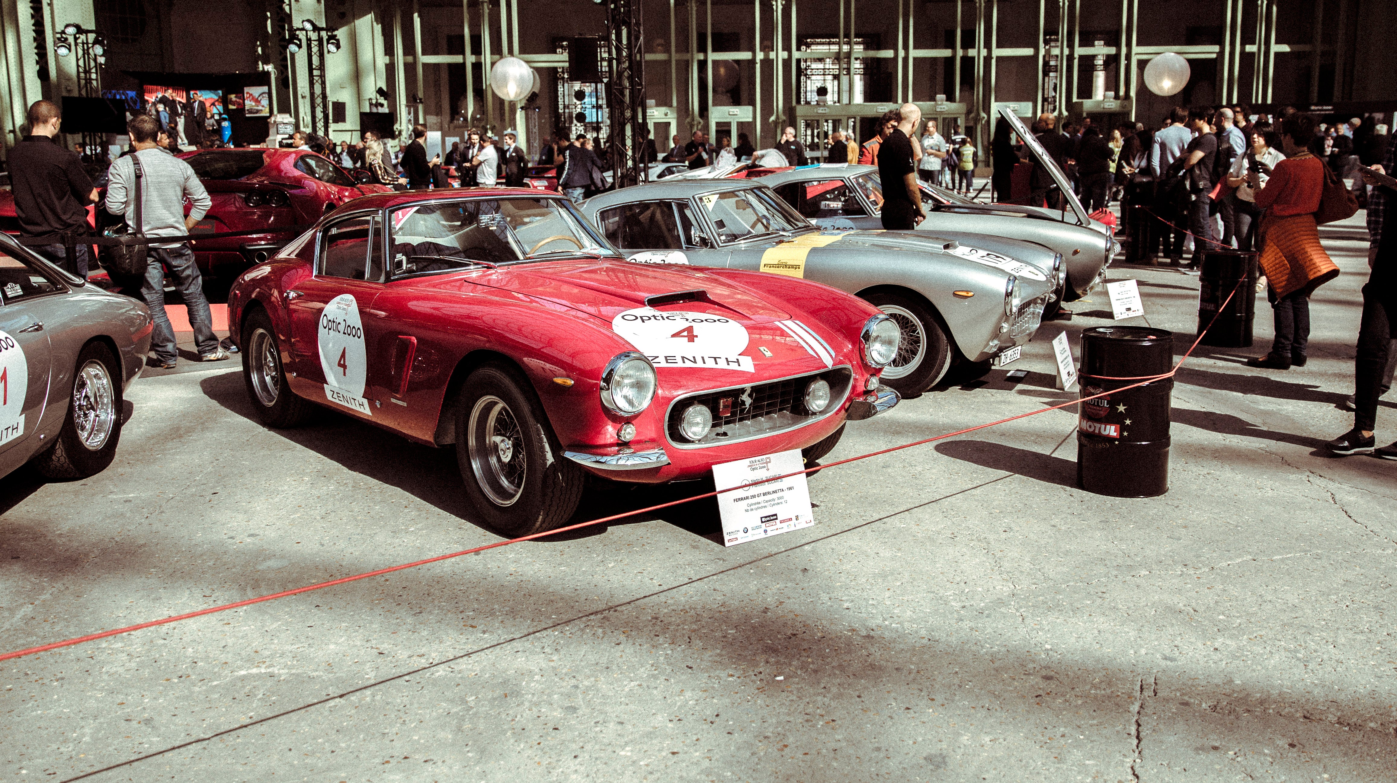 Une grande foule de personnes observant des supercars classiques garées dans une rue de village lors du Tour Auto Optic 2000.